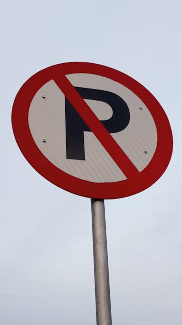 A rectangular white metal sign mounted on a grey wooden door or wall with visible panel lines and a horizontal support beam, displaying the message 'NO PARKING DAY OR NIGHT' in bold black uppercase letters. The sign is attached with four metal screws, one in each corner. The background suggests an outdoor environment, potentially on a garage door or building exterior. This sign is positioned near the top of the door or wall section. The scene is well-lit with natural lighting, highlighting the sign's clear, high-contrast text. The image reflects aspects of parking restrictions that could impact home relocation or furniture transport logistics, as part of a broader discussion on house removals, managed by a professional service like Man with Van Keston, who might need to consider street closure rules for efficient moving services near Keston and Bromley.